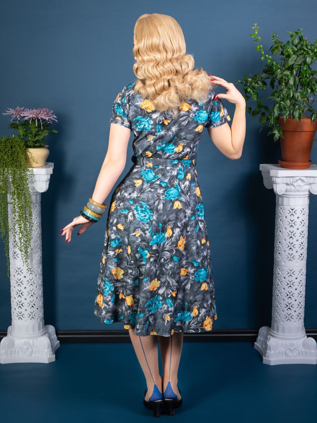 back view of retro 1950s grey dress with  floral print in burnt orange and turquoise worn with blue seamed stockings