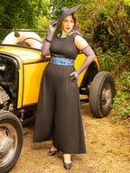 Woman in a vintage black beach pyjamas standing next to a yellow vintage car in a forest setting