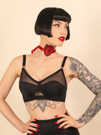 Woman wearing a black bralette with tattoos and red lipstick against a beige background