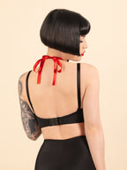 Woman wearing black retro lingerie with a red ribbon in the back against a beige background