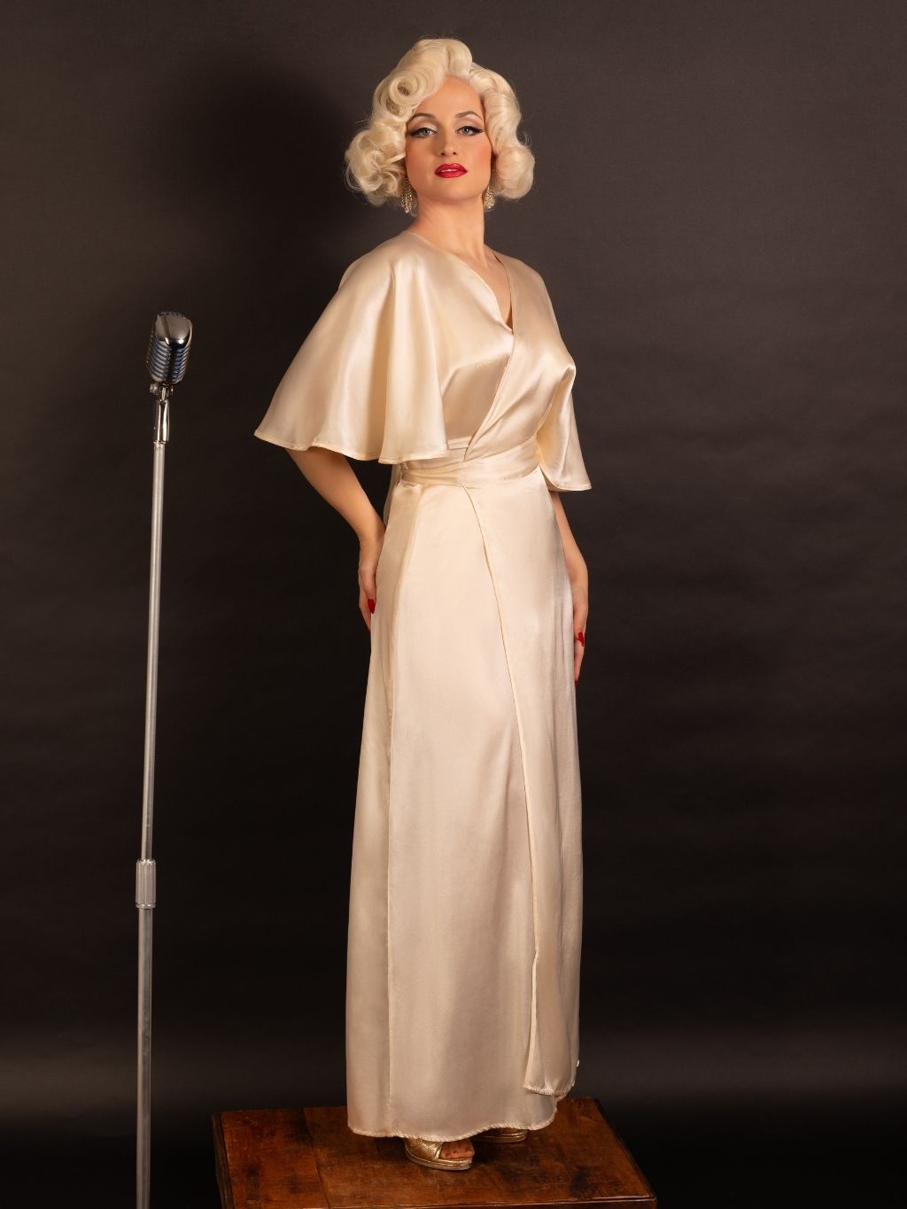 Person in a vintage-style peach satin robe standing next to a microphone on a dark background