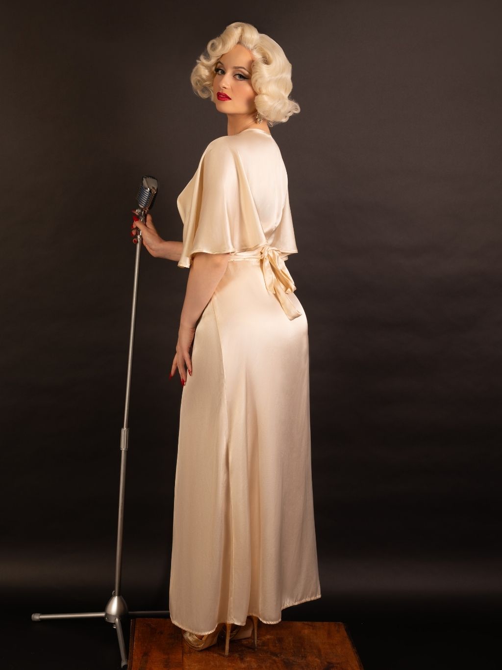 Woman in a vintage peach satin robe holding a microphone against a dark background