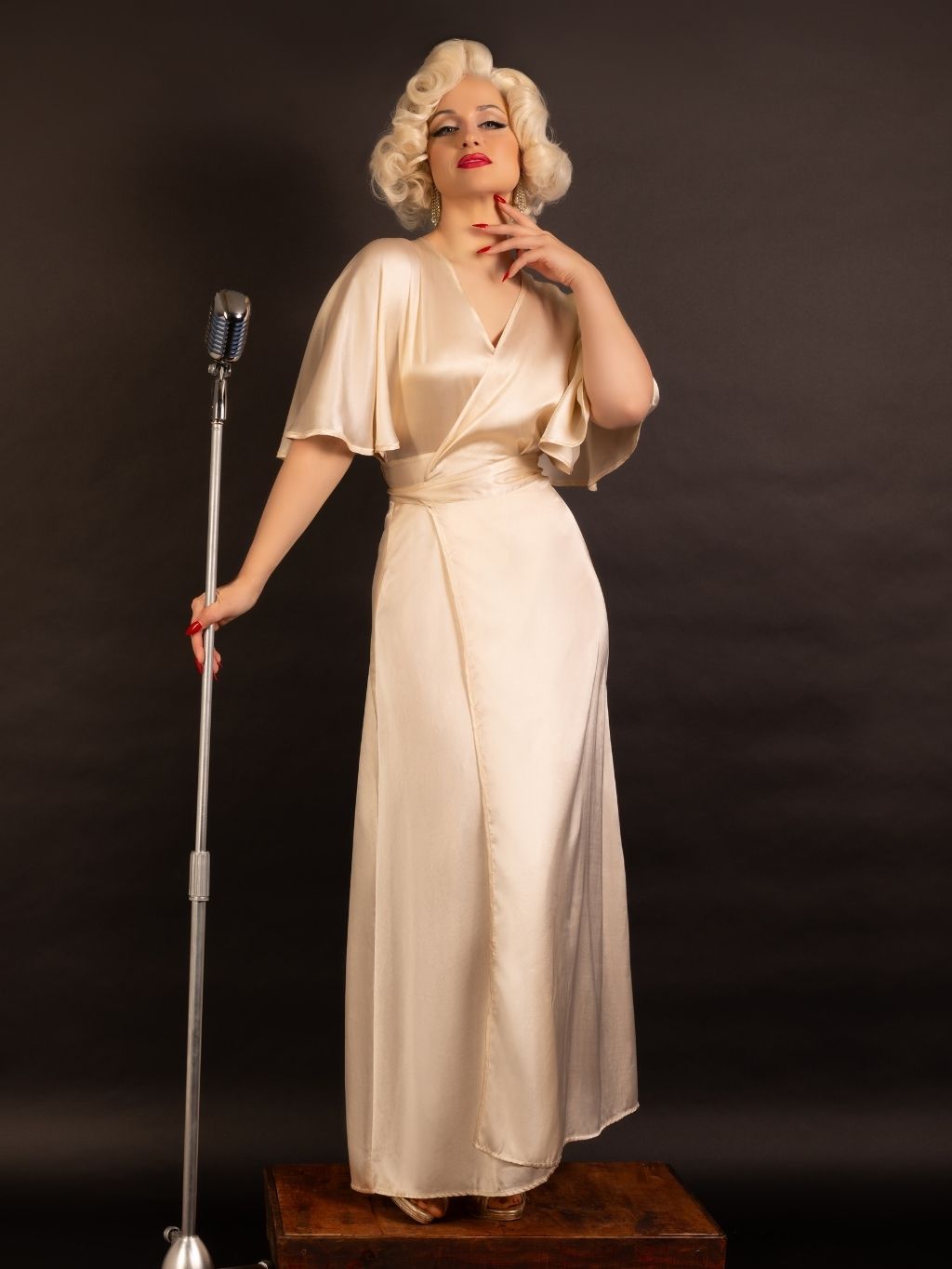 Woman in a vintage-style peach satin robe standing next to a microphone on a dark background