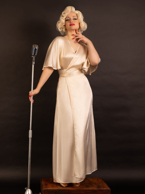 Woman in a vintage-style peach satin robe standing next to a microphone on a dark background