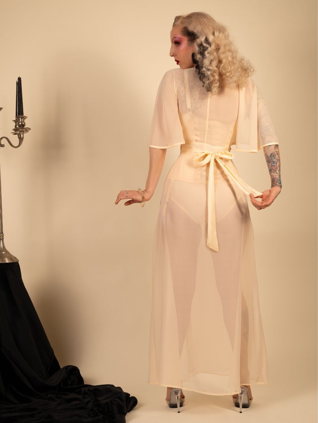 Woman wearing a sheer beige dress with a belt in a studio setting.