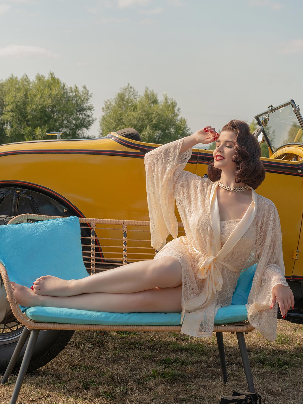 Woman in a peach lace kimono sitting on a blue chair in front of a vintage car