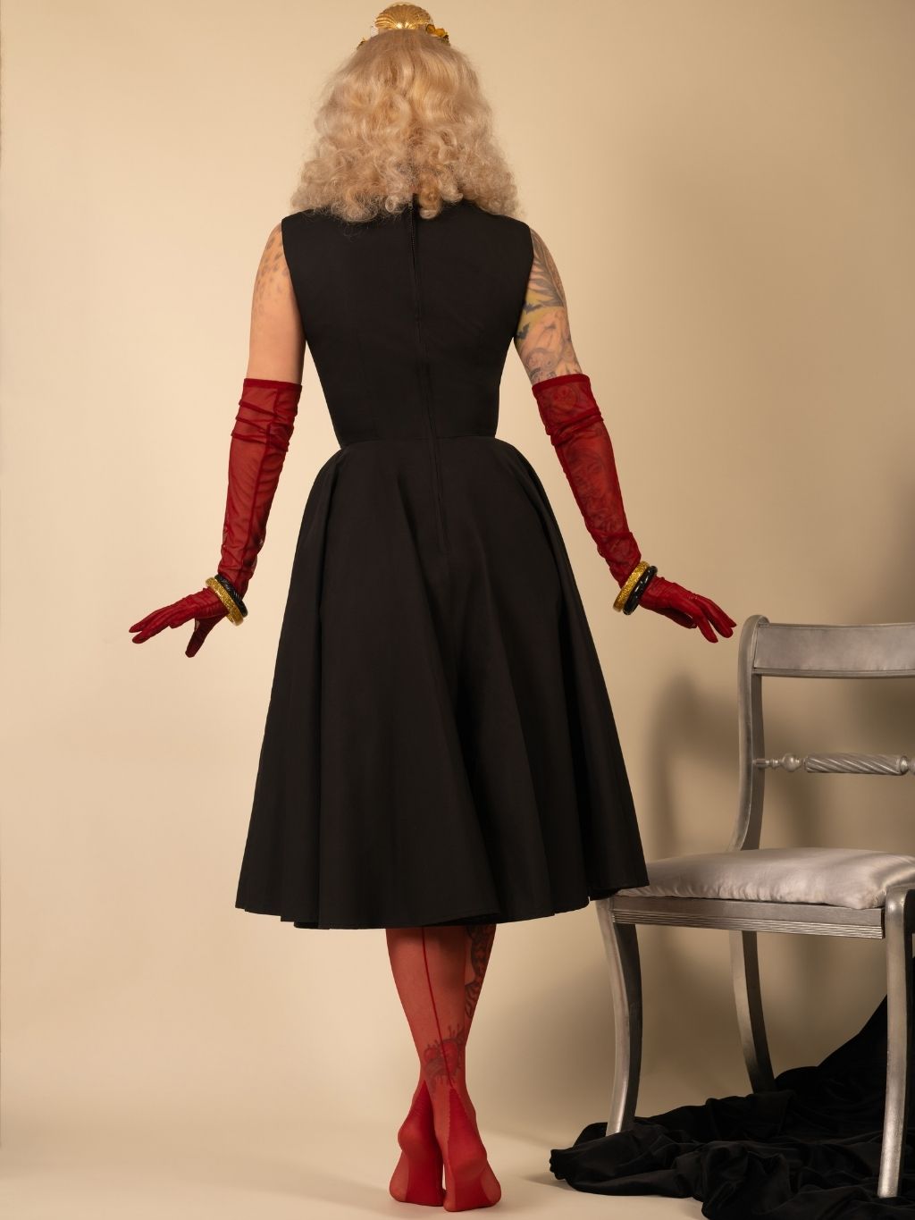 Person wearing a black dress with red gloves and stockings against a beige background