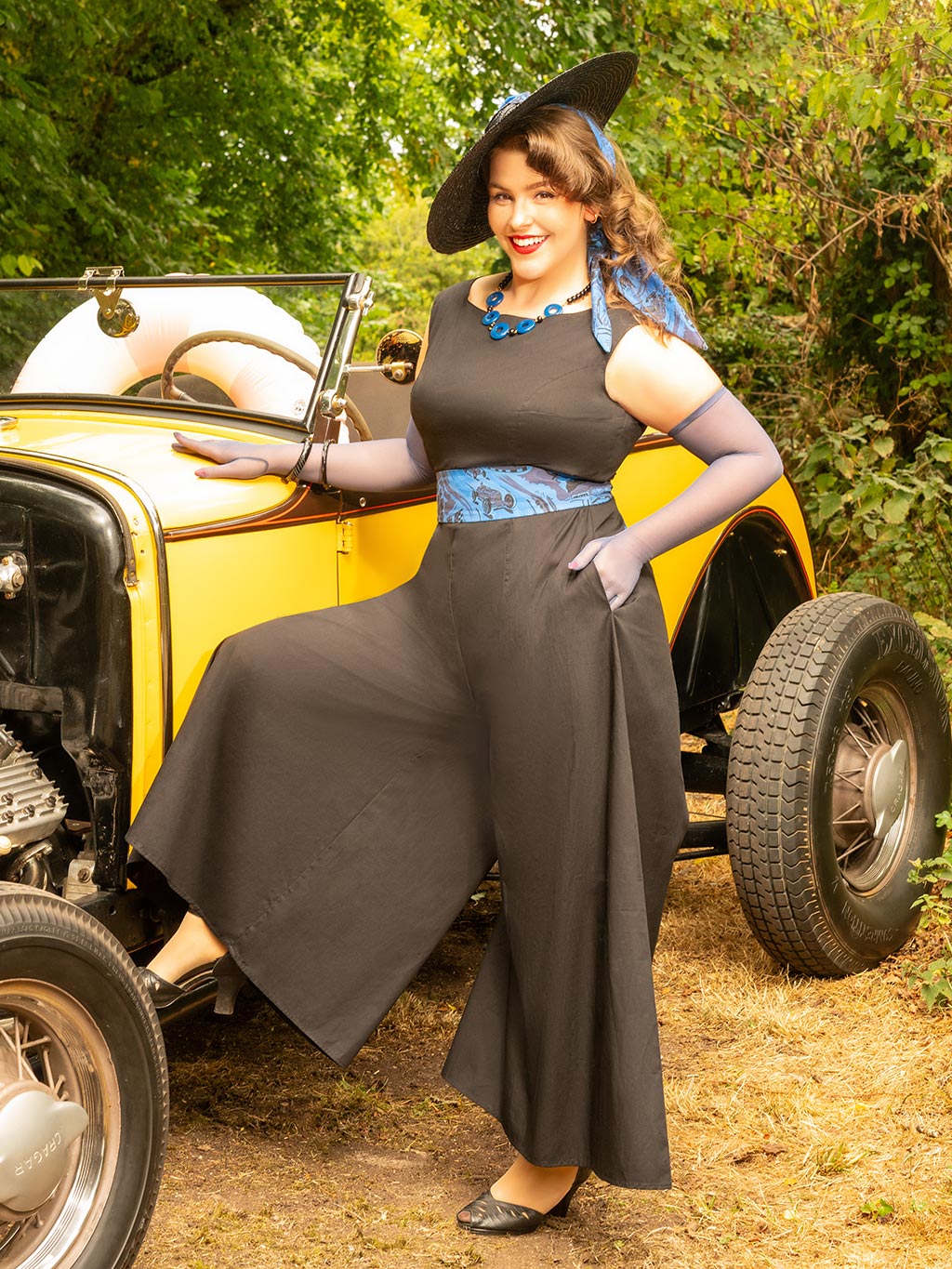 Woman in vintage black beach pyjamas sitting on a classic car outdoors