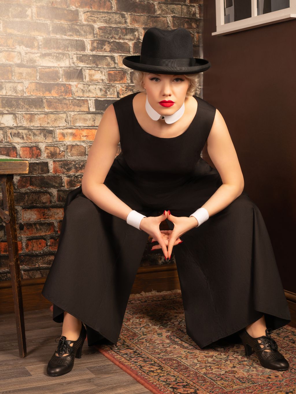 Woman in retro black beach pyjamas and hat sitting against a brick wall
