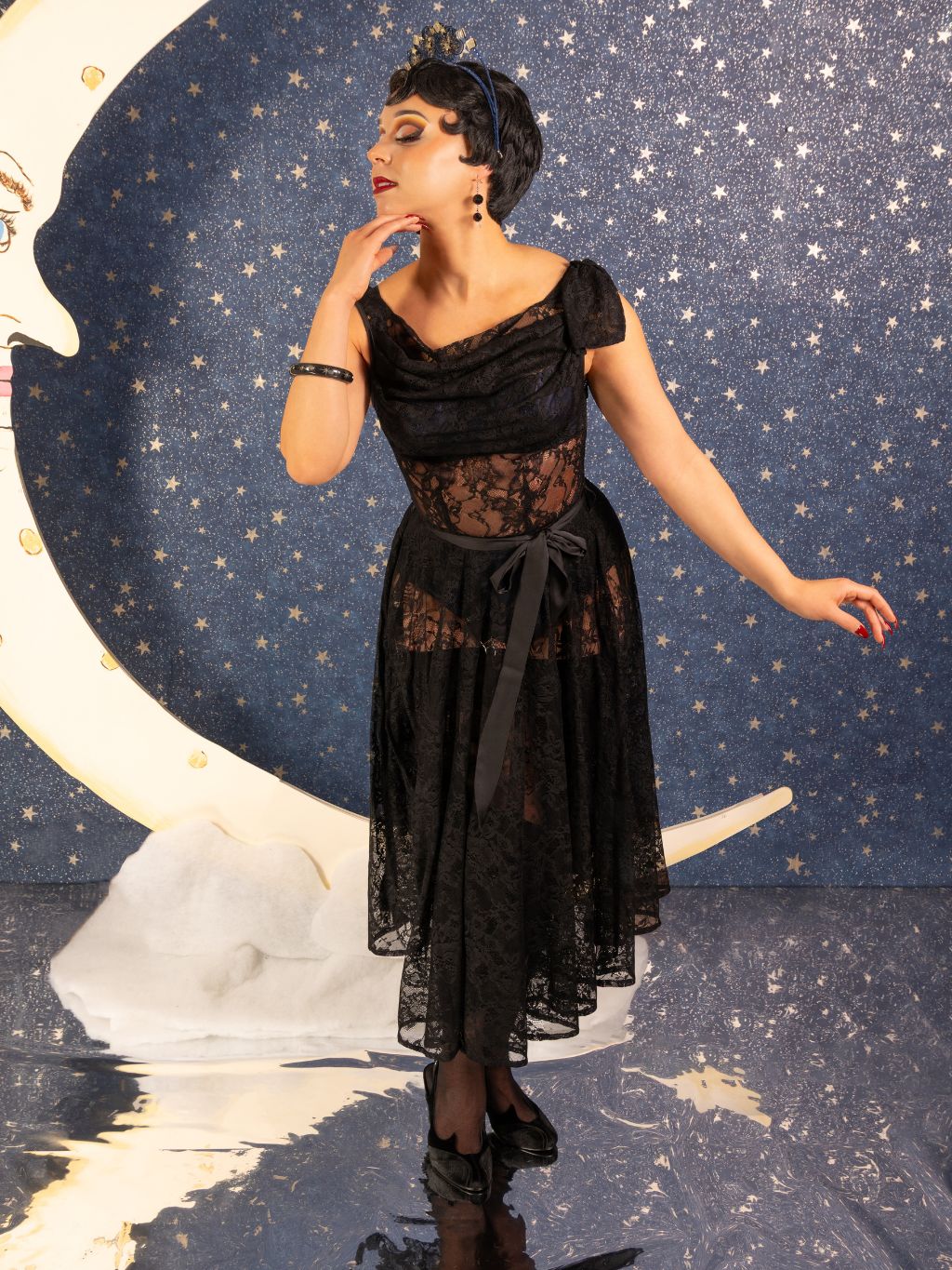 Woman in a black lace dress against a starry night sky with a moon and cloud backdrop