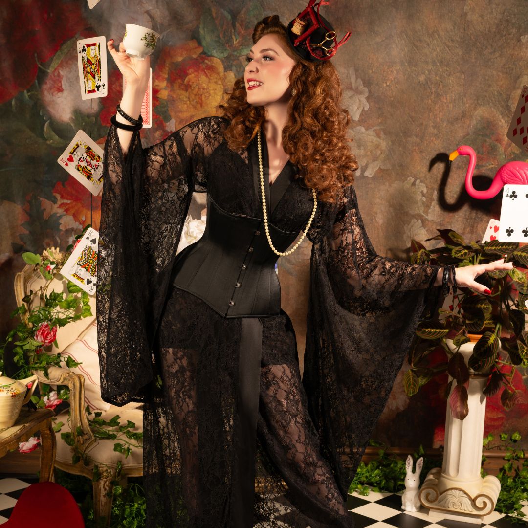 Woman in a theatrical costume holding a card and cup, with a fantasy-themed background.