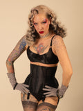 Woman wearing a black waist cincher and gloves against a beige background