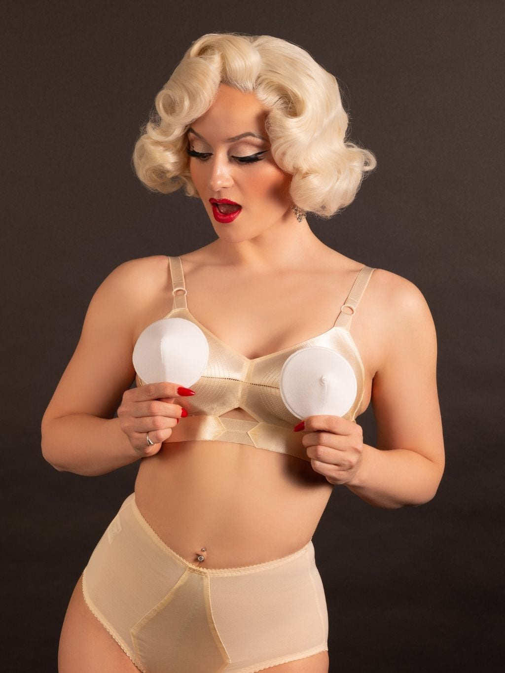 Person wearing a beige bra and underwear set holding white circular bullet bra pads against a dark background