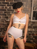Woman wearing a retro white bra and panties set against a brick wall.